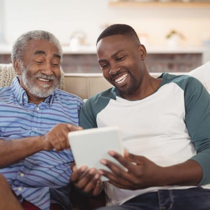 Father and son showing user interface design for seniors using tablet on couch