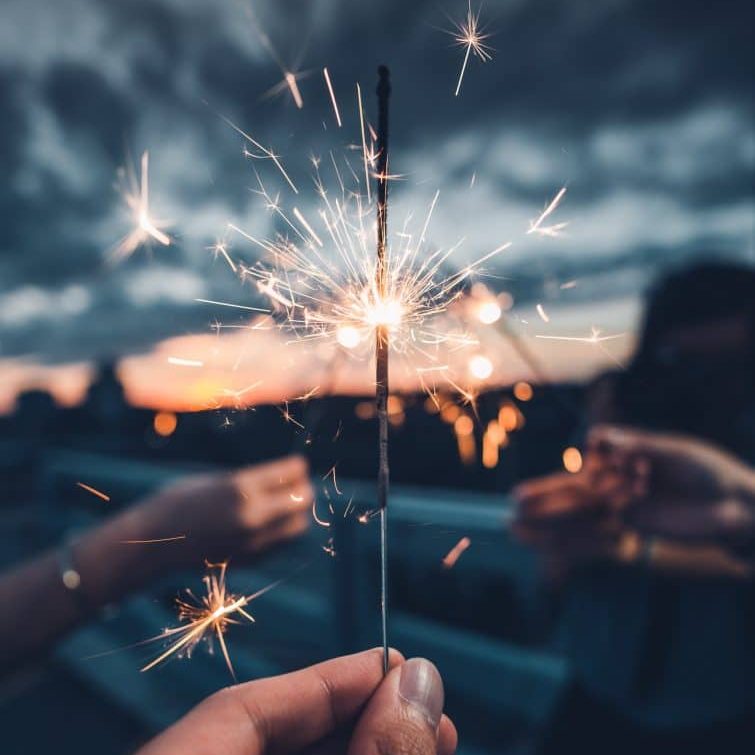 Hand holding a lit sparkler in front of a sunset
